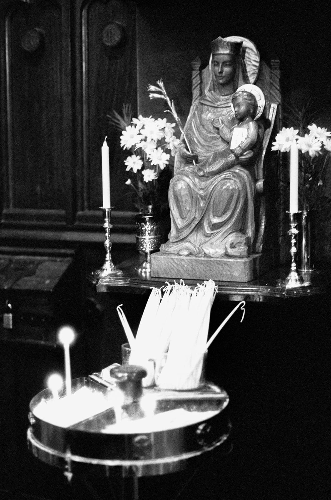Black and white photo of a statue of the Virgin and Child with white flowers and candles at a side shrine of the church, on 35mm film