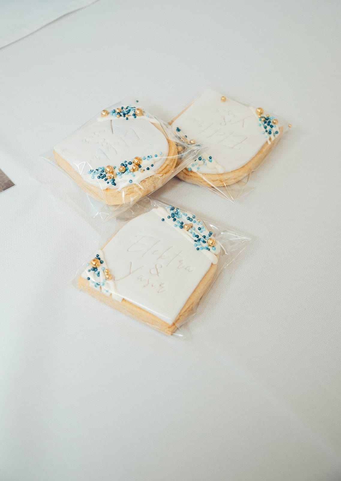 Iced biscuits with Elektra and Yasir’s names and blue and gold sprinkles, in clear bags