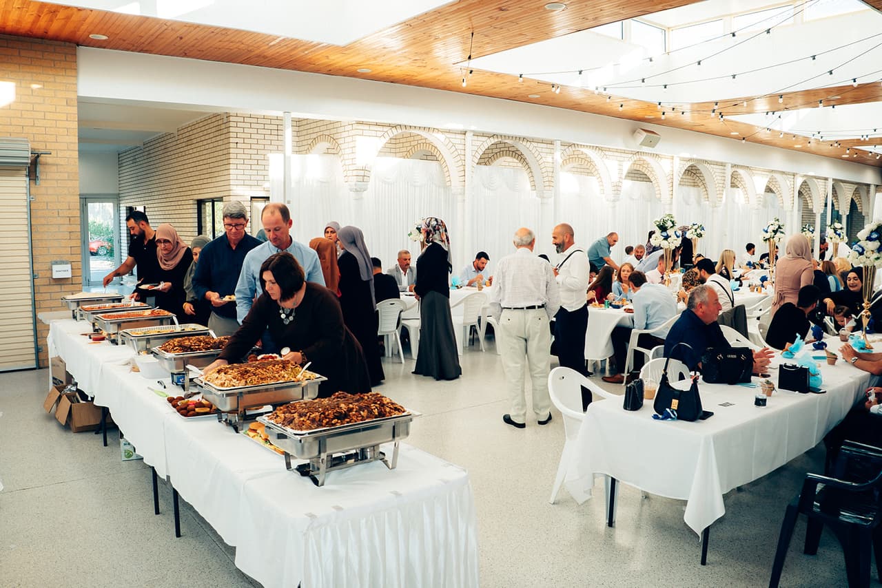 The buffet of hot food along one side of the hall, guests filling their plates while others sit at the tables