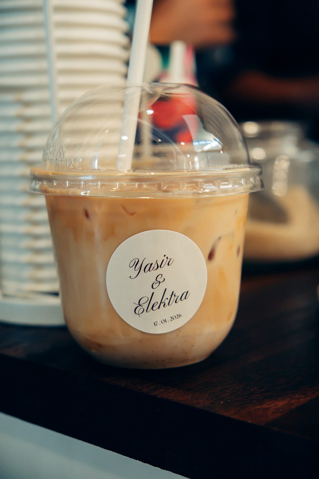 An iced coffee in a cup with a round sticker bearing Yasir and Elektra’s names and the date