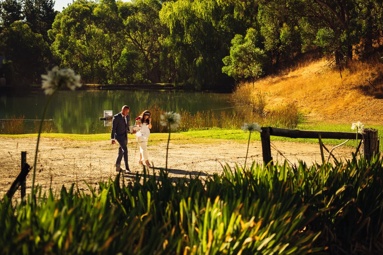 Kim and Ben walking by the pond below a golden hillside, agapanthus in the foreground
