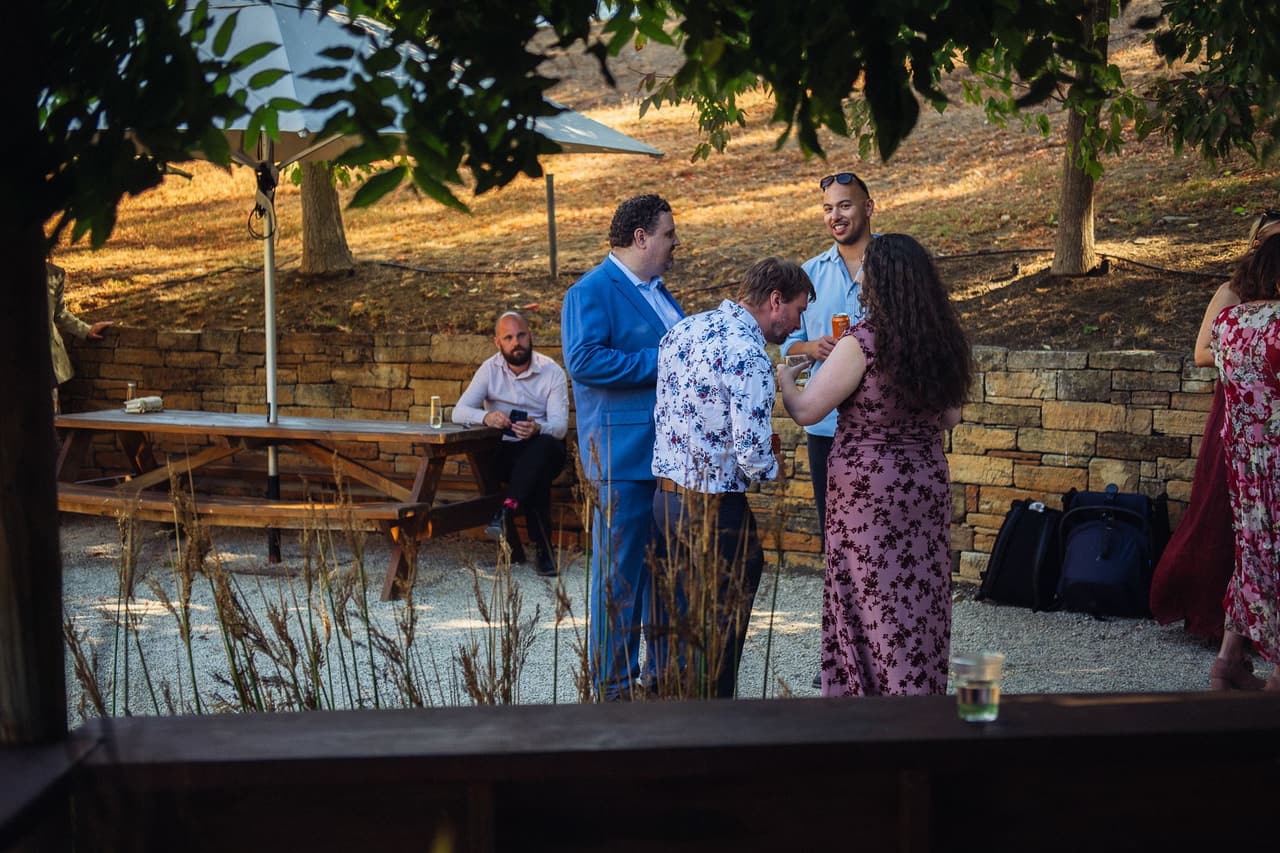 The gravel courtyard beside the Boatshed, with picnic tables, a dry-stone wall and white umbrellas, guests chatting over drinks