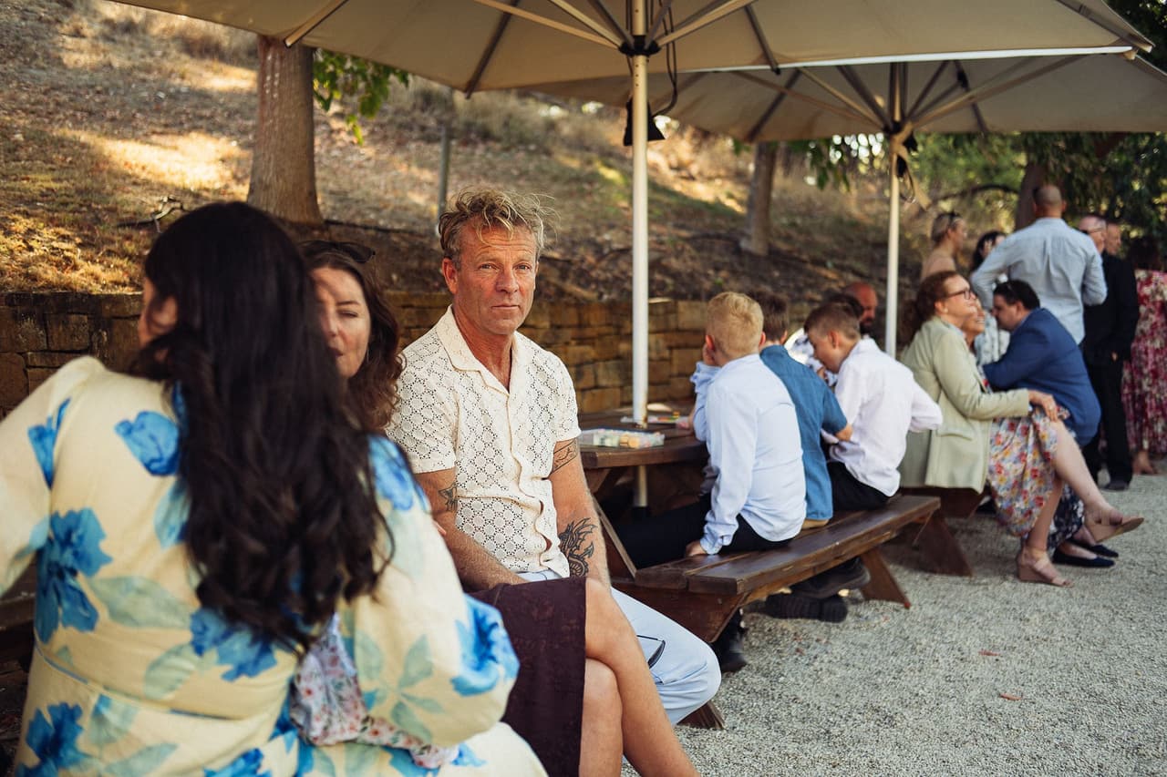 Guests sitting at the timber picnic tables under the umbrellas beside the stone wall