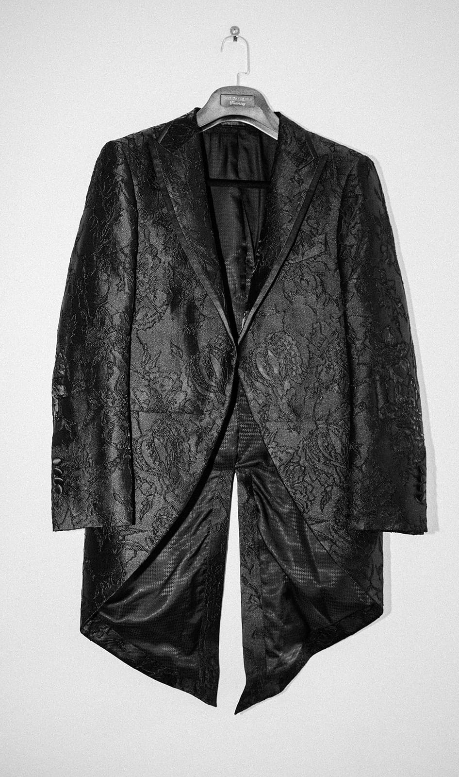 Jordan’s black brocade tailcoat hanging on a white door