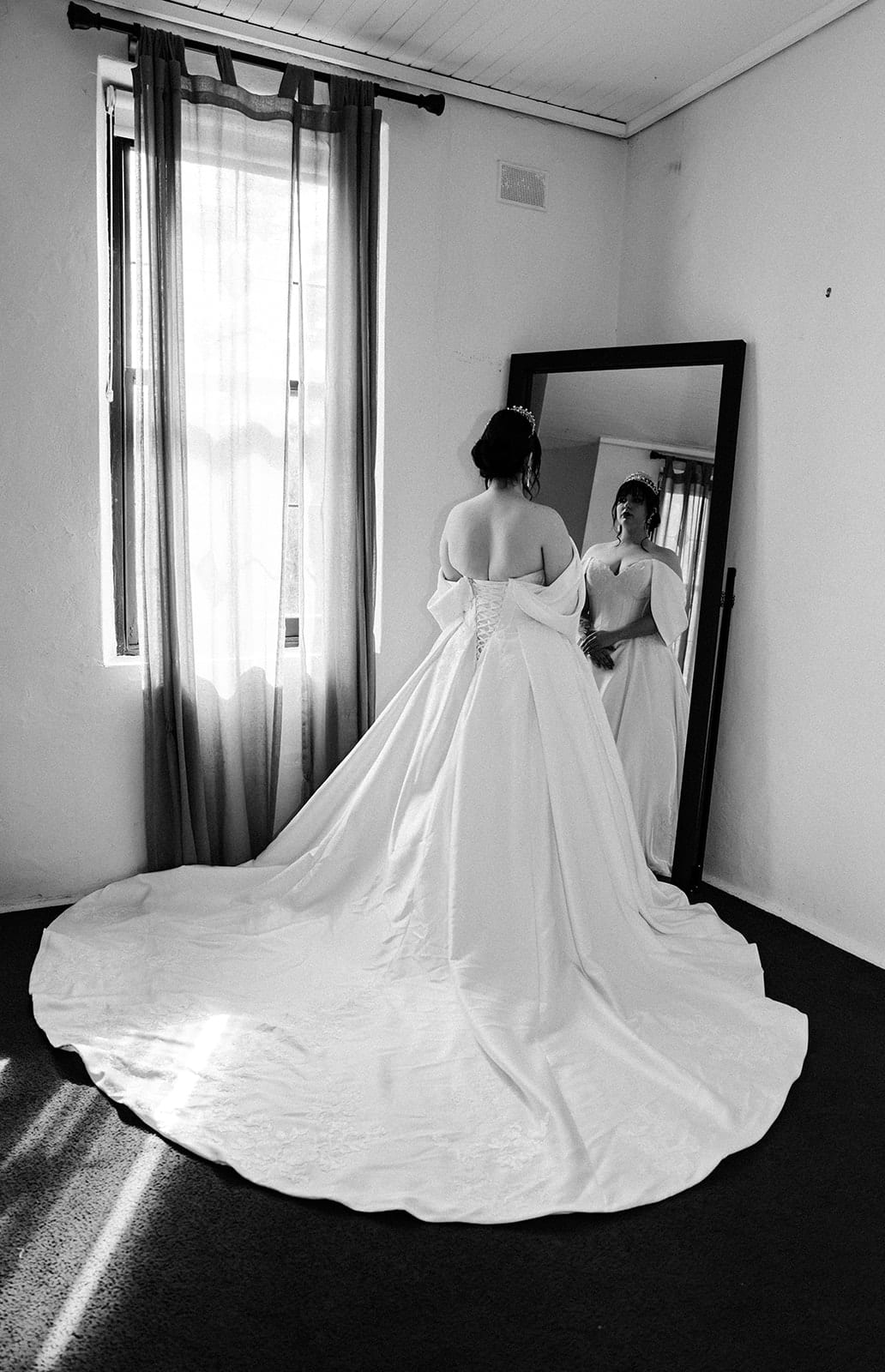 Black and white photo of Porscha at the mirror in a white room, her train spread across the floor