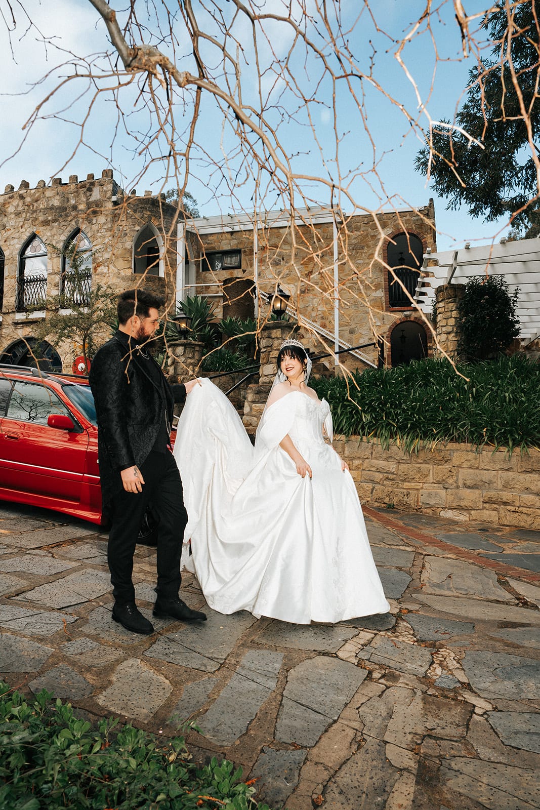 Porscha and Jordan in the castle courtyard beside a red vintage car, the battlements behind them