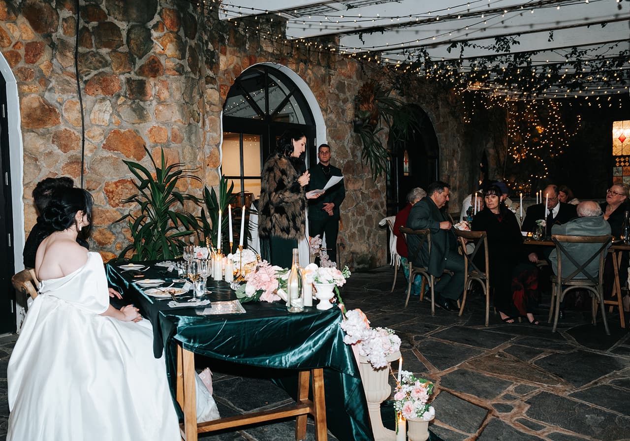 Porscha at the long tables during the speeches under the covered stone terrace, fairy lights overhead