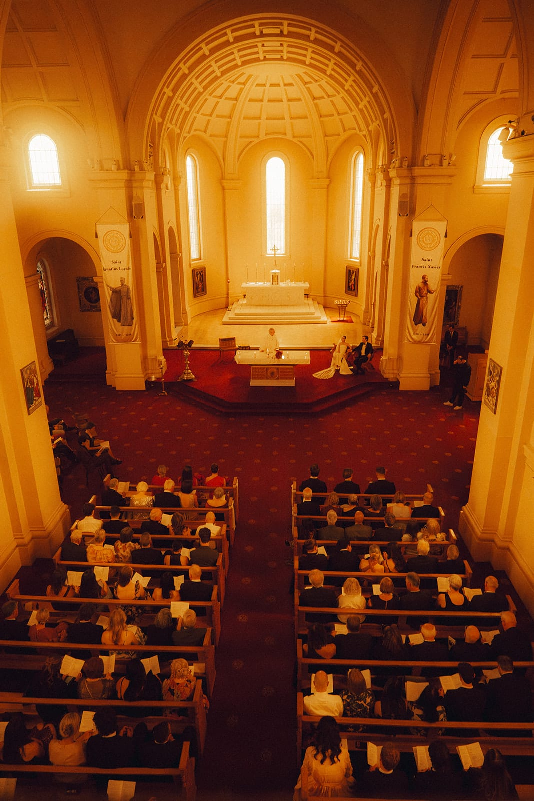 The full chapel seen from the back gallery during the ceremony, the red aisle running between the pews to the altar