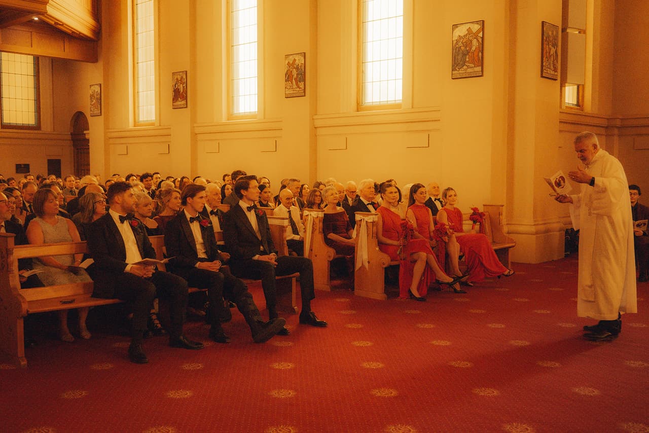 The priest speaking to the bridal party in the front pews, guests filling the rows behind them