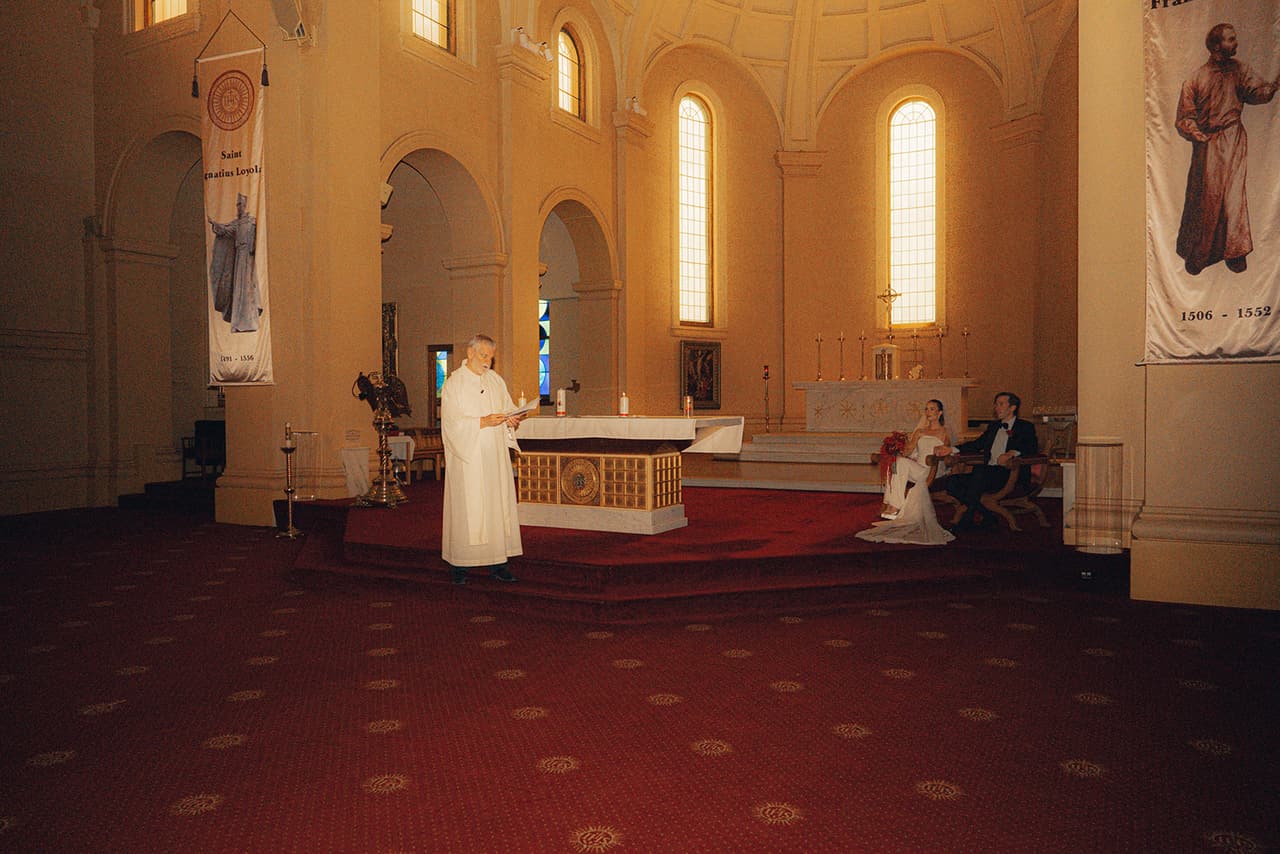 The sanctuary during the ceremony, the priest at the altar and Kira and Nick seated to one side beneath the arched windows