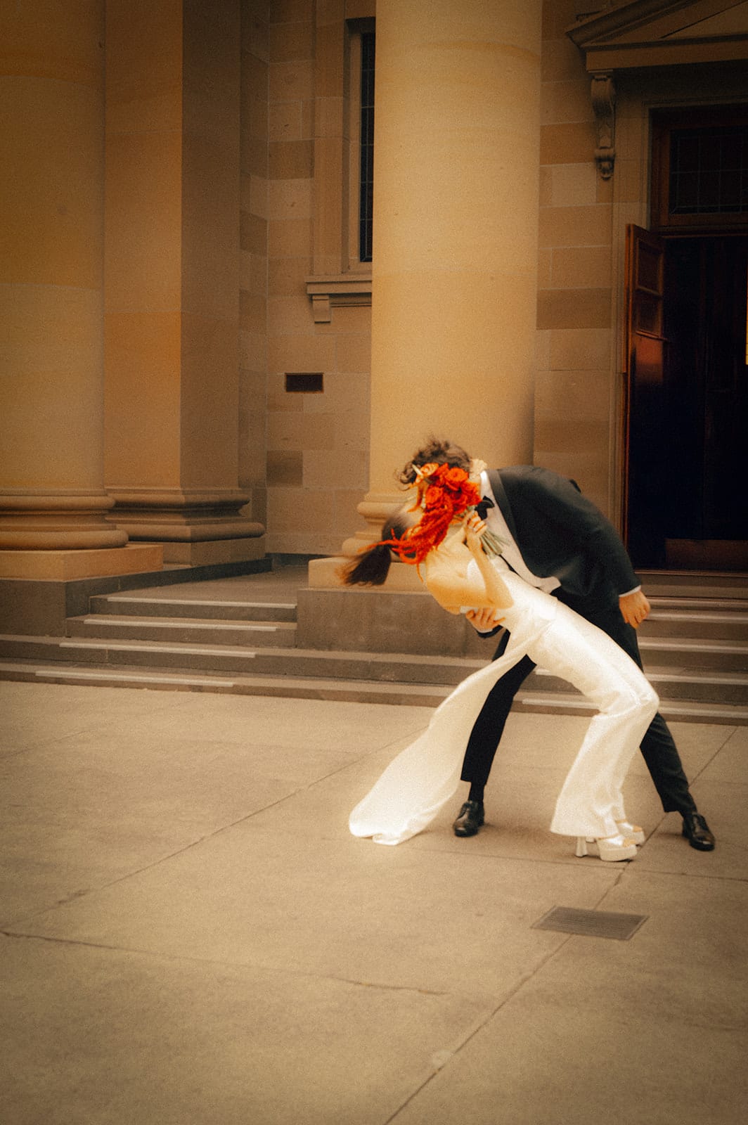 Nick dipping Kira on the chapel steps beneath the sandstone portico