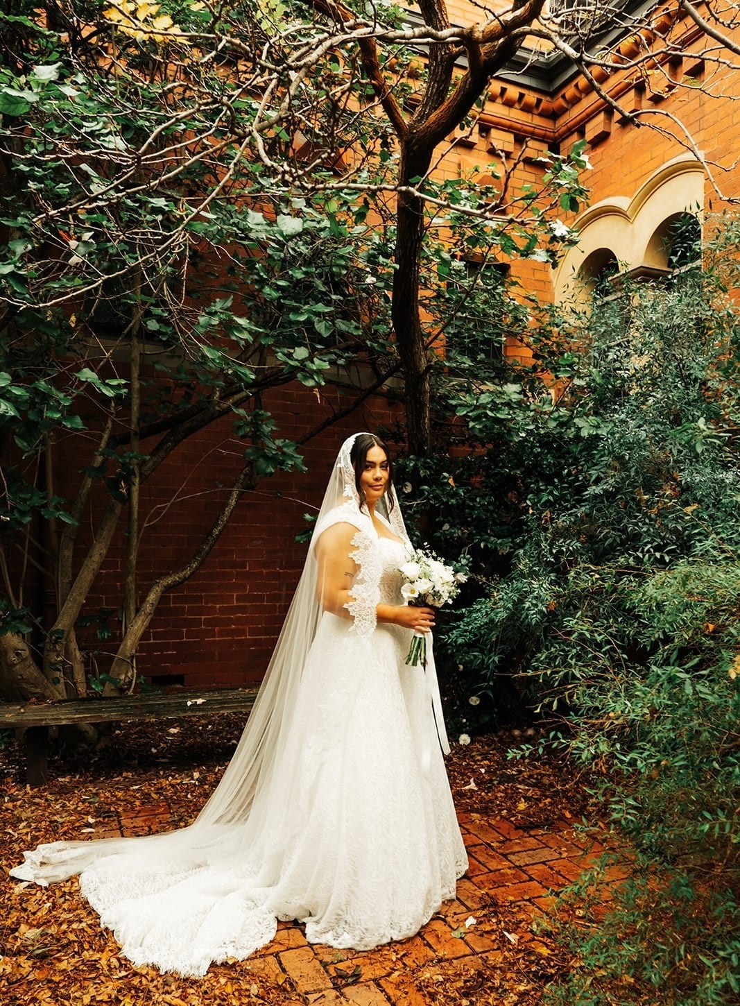 Ashley standing among the trees with her train spread over the fallen leaves