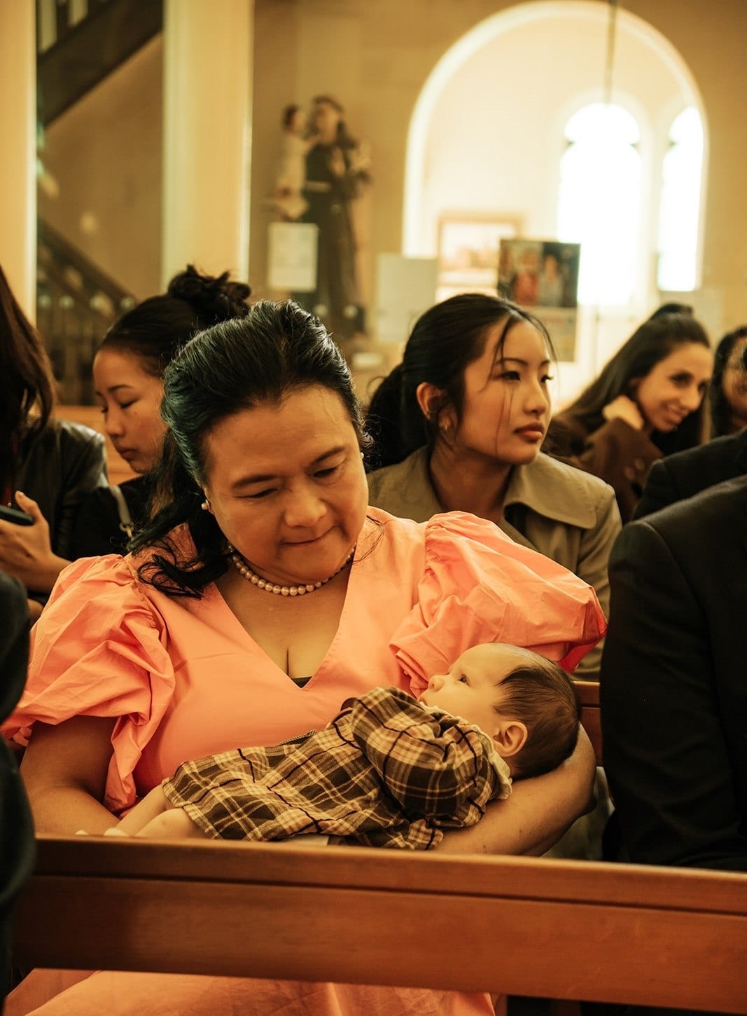 A guest in a peach dress cradling a sleeping baby in the pews