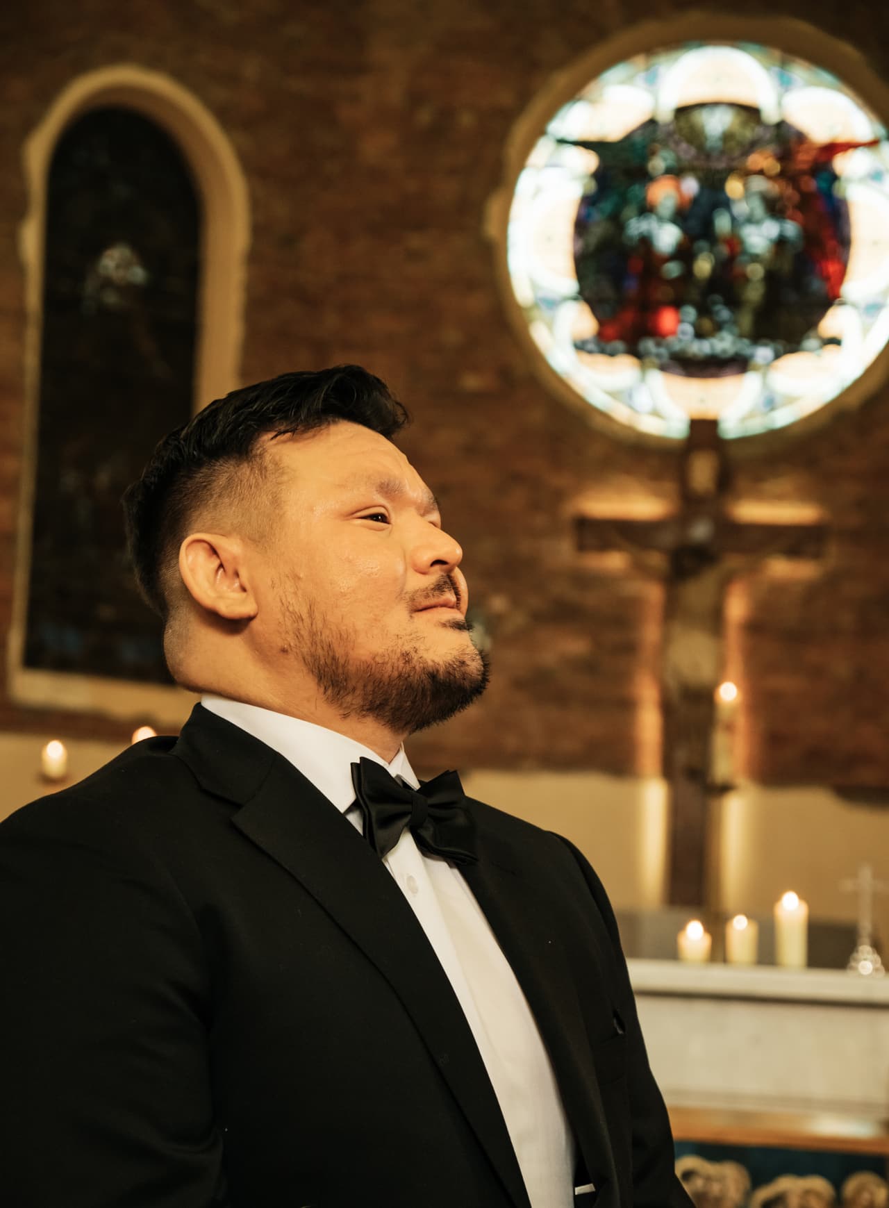 Bryan in a black tuxedo and bow tie looking up and smiling beside the altar