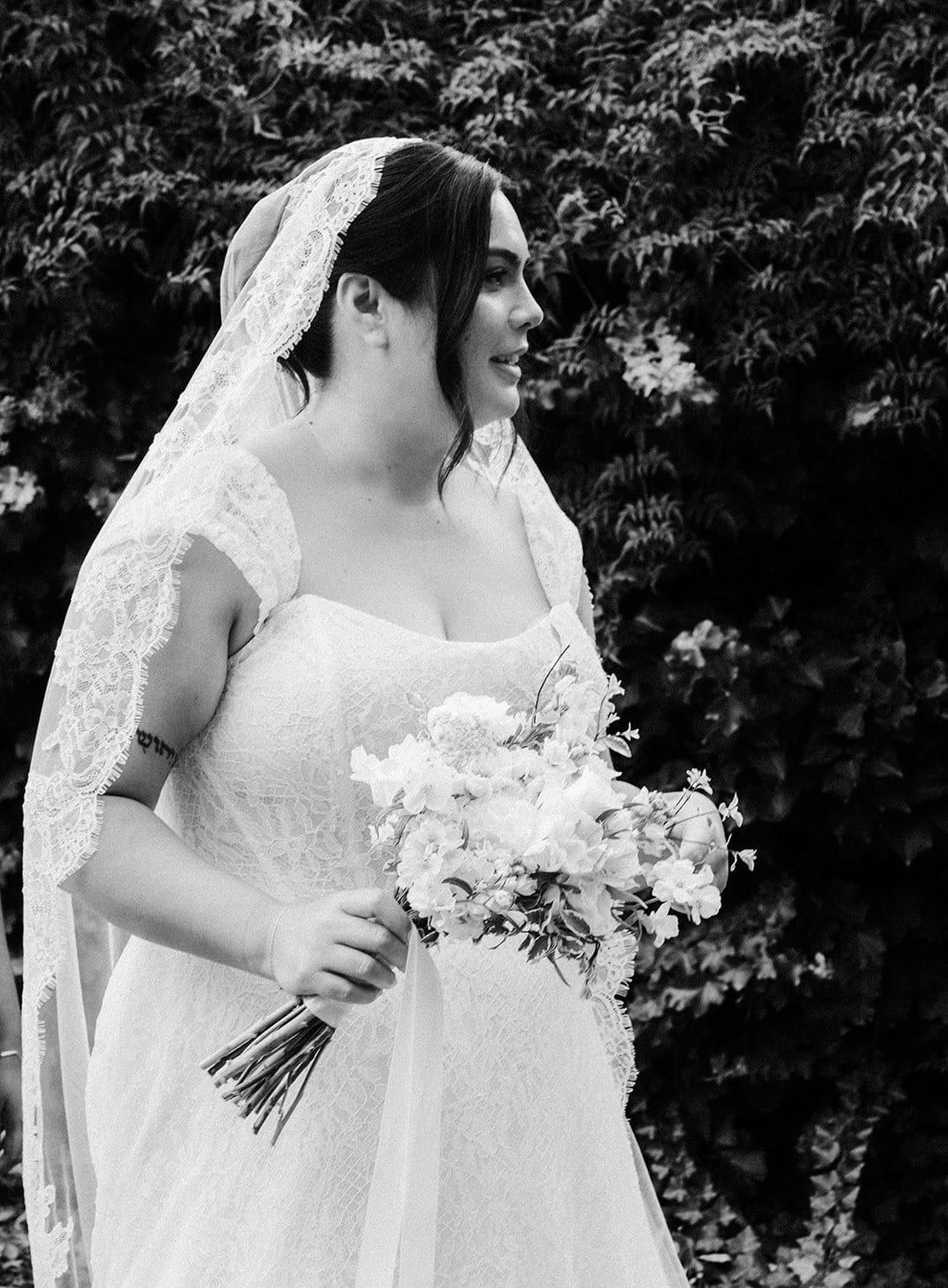 Black and white photo of Ashley holding her white bouquet and looking away