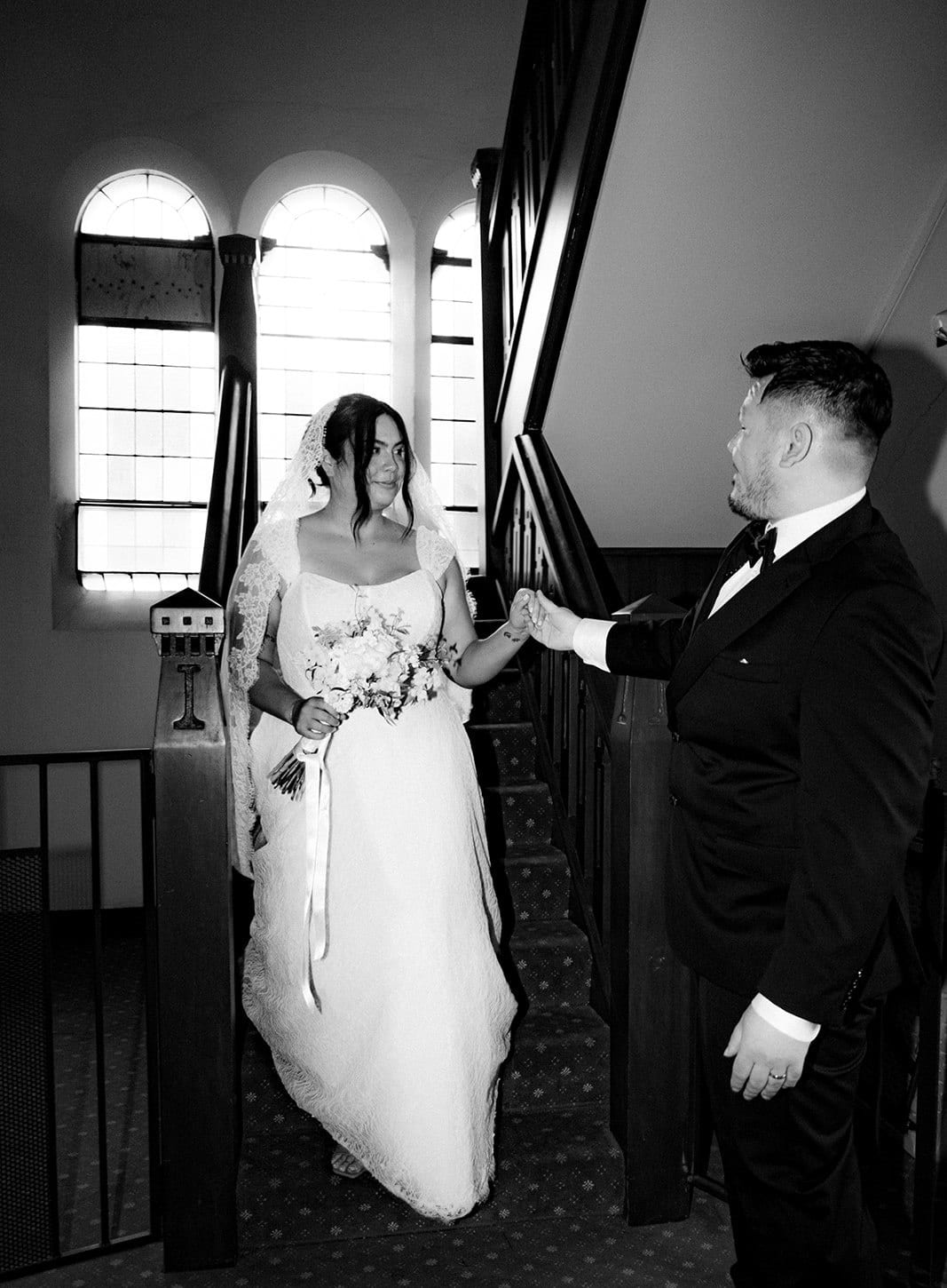 Black and white photo of Bryan holding Ashley’s hand as she comes down the stairs