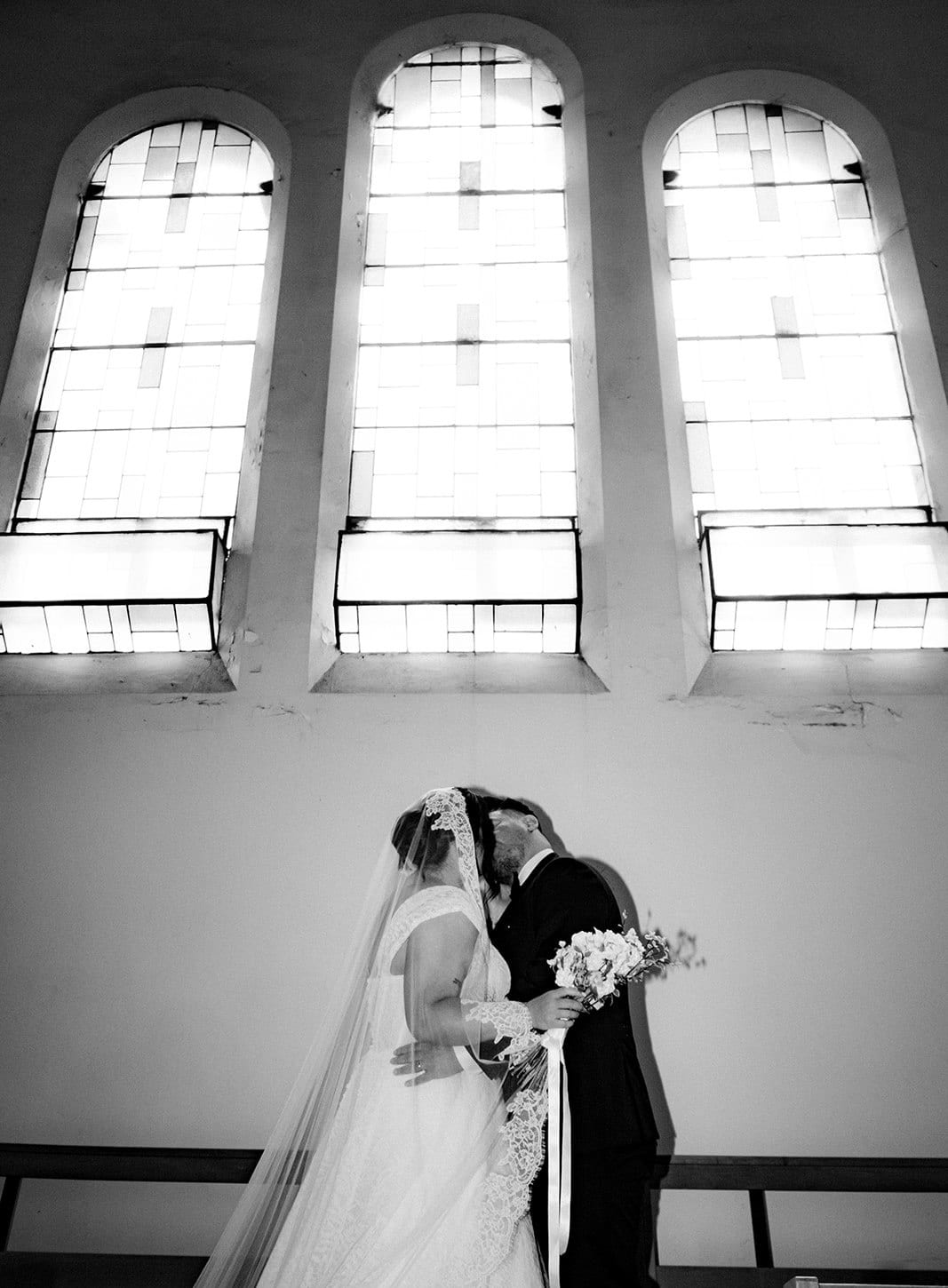 Black and white photo of Ashley and Bryan kissing in front of the tall windows