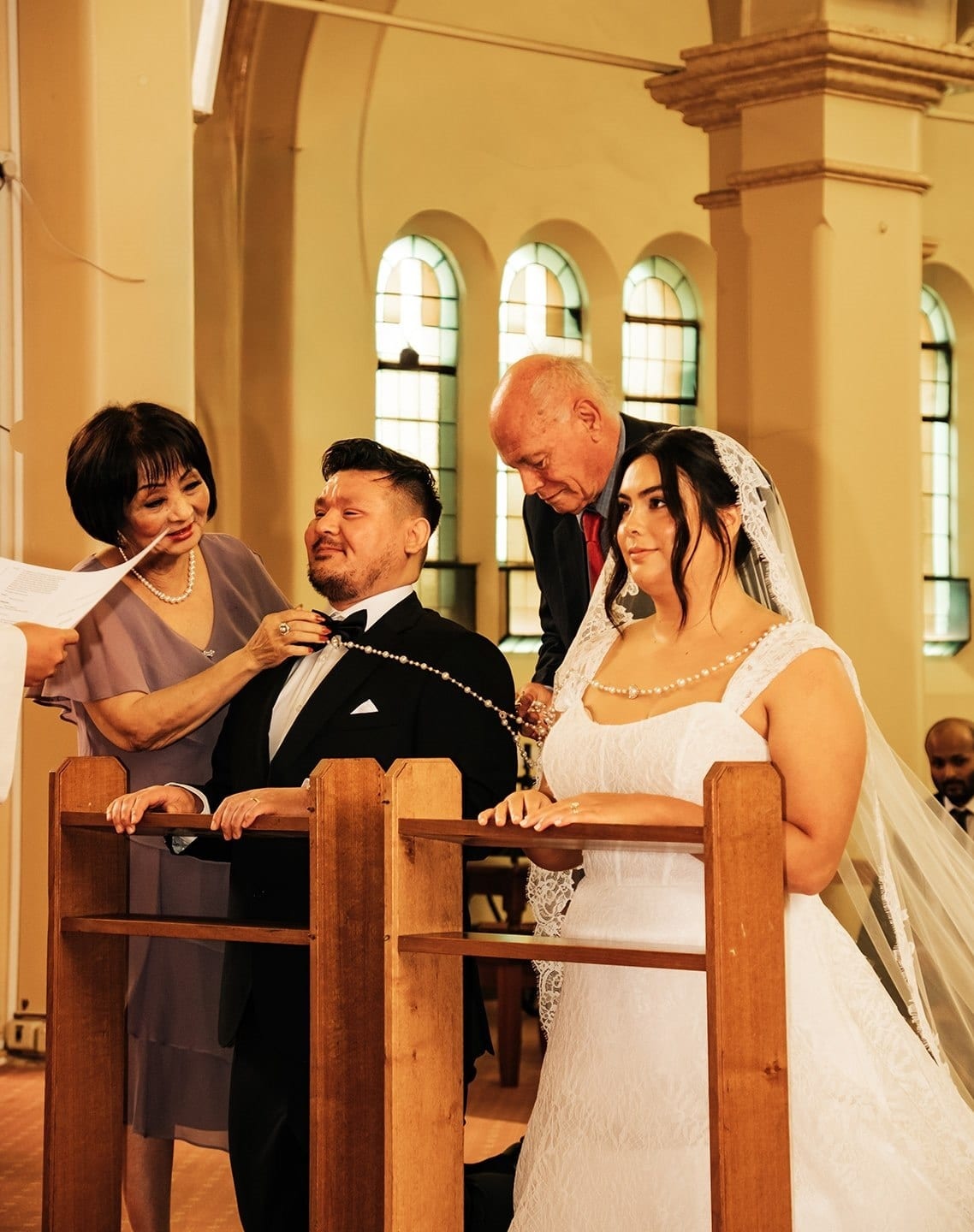Two family members placing a cord of rosary beads over Ashley and Bryan at the kneelers