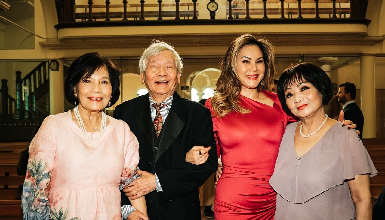 Four family members in pink, red and lilac laughing arm in arm in the church before the ceremony