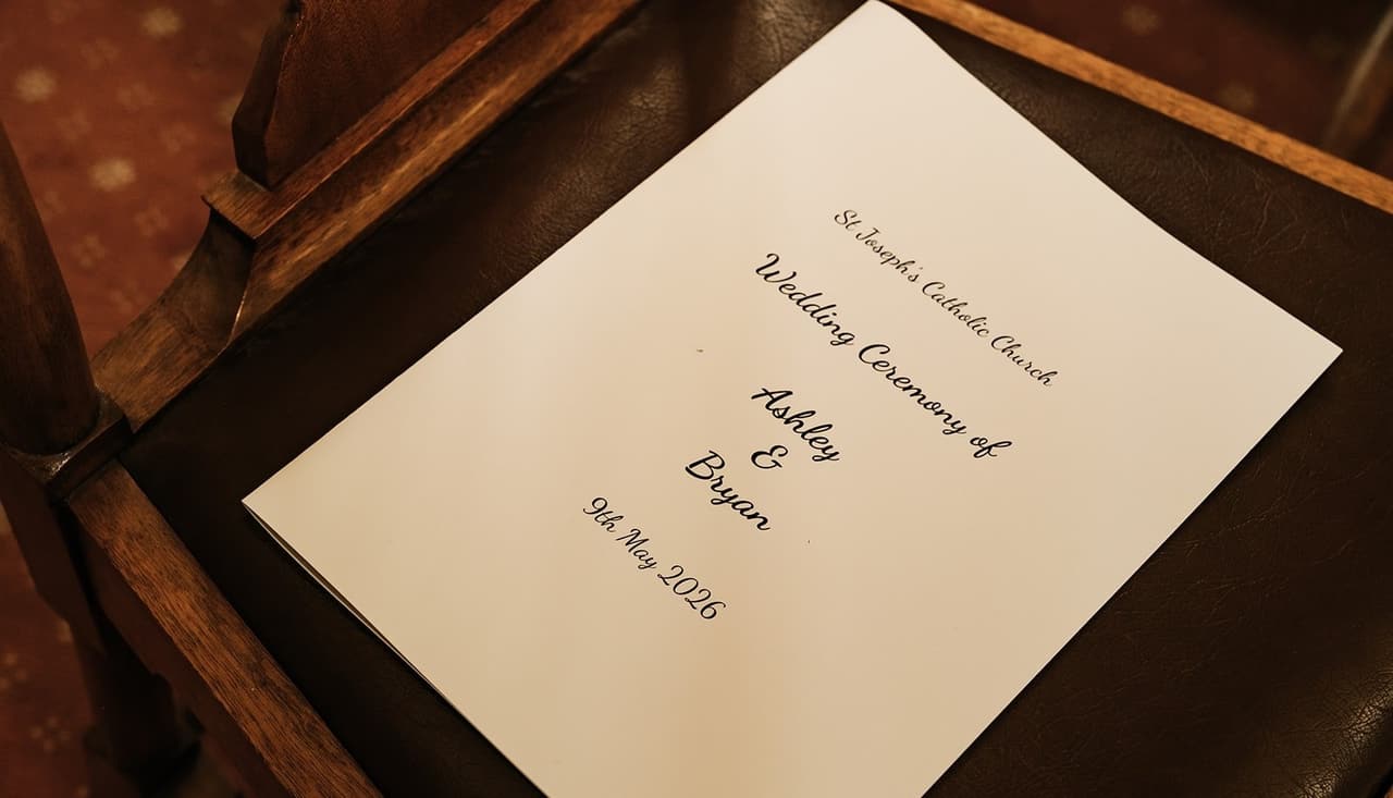 The order of service for Ashley and Bryan’s wedding resting on a timber pew