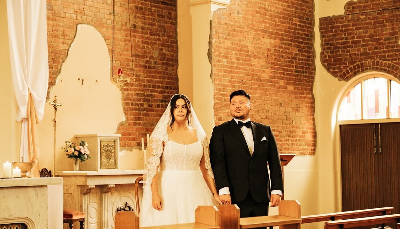 Ashley and Bryan standing behind the timber kneelers during the ceremony