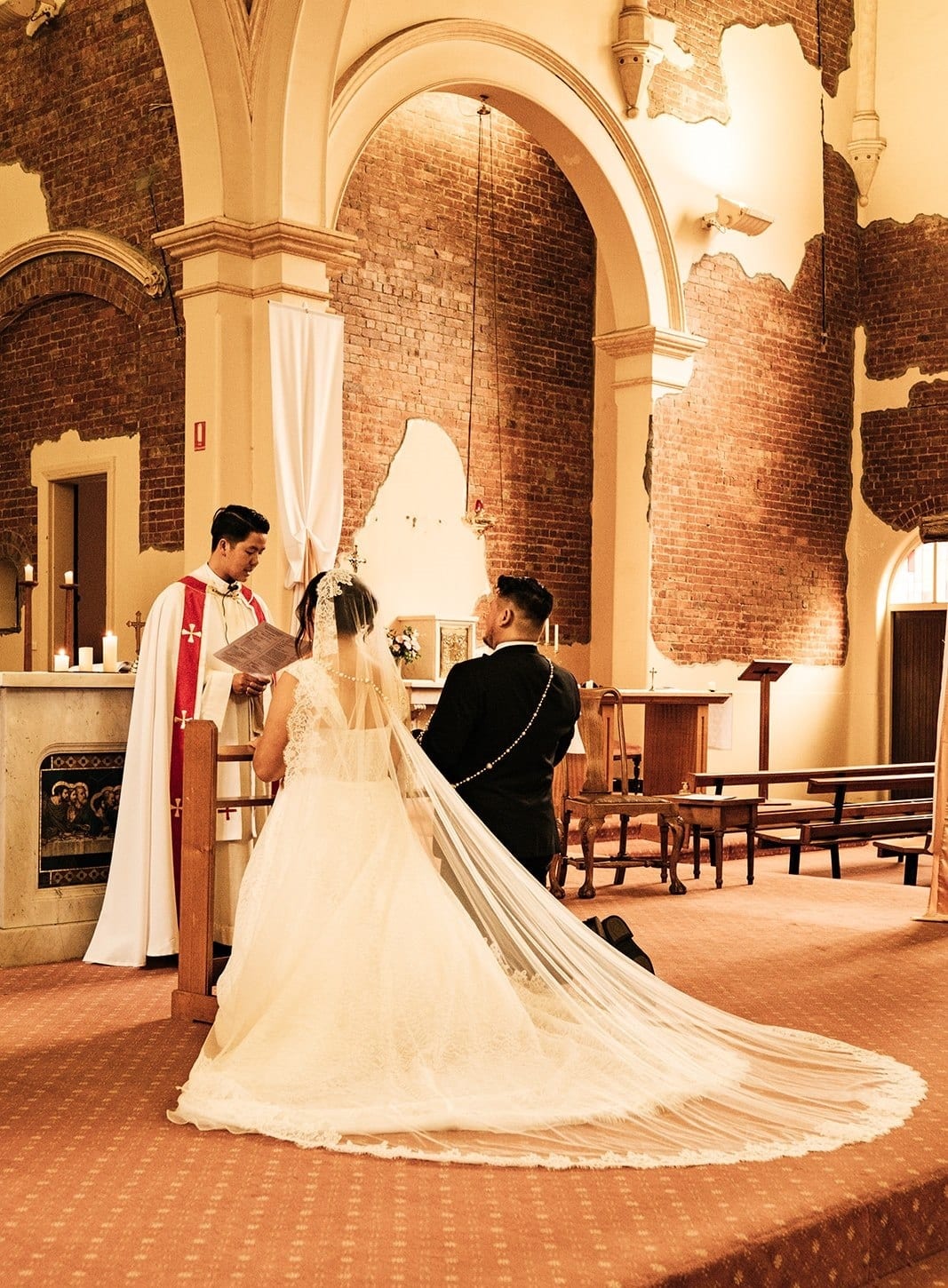 Ashley’s veil and train spread across the sanctuary floor as they stand before the priest