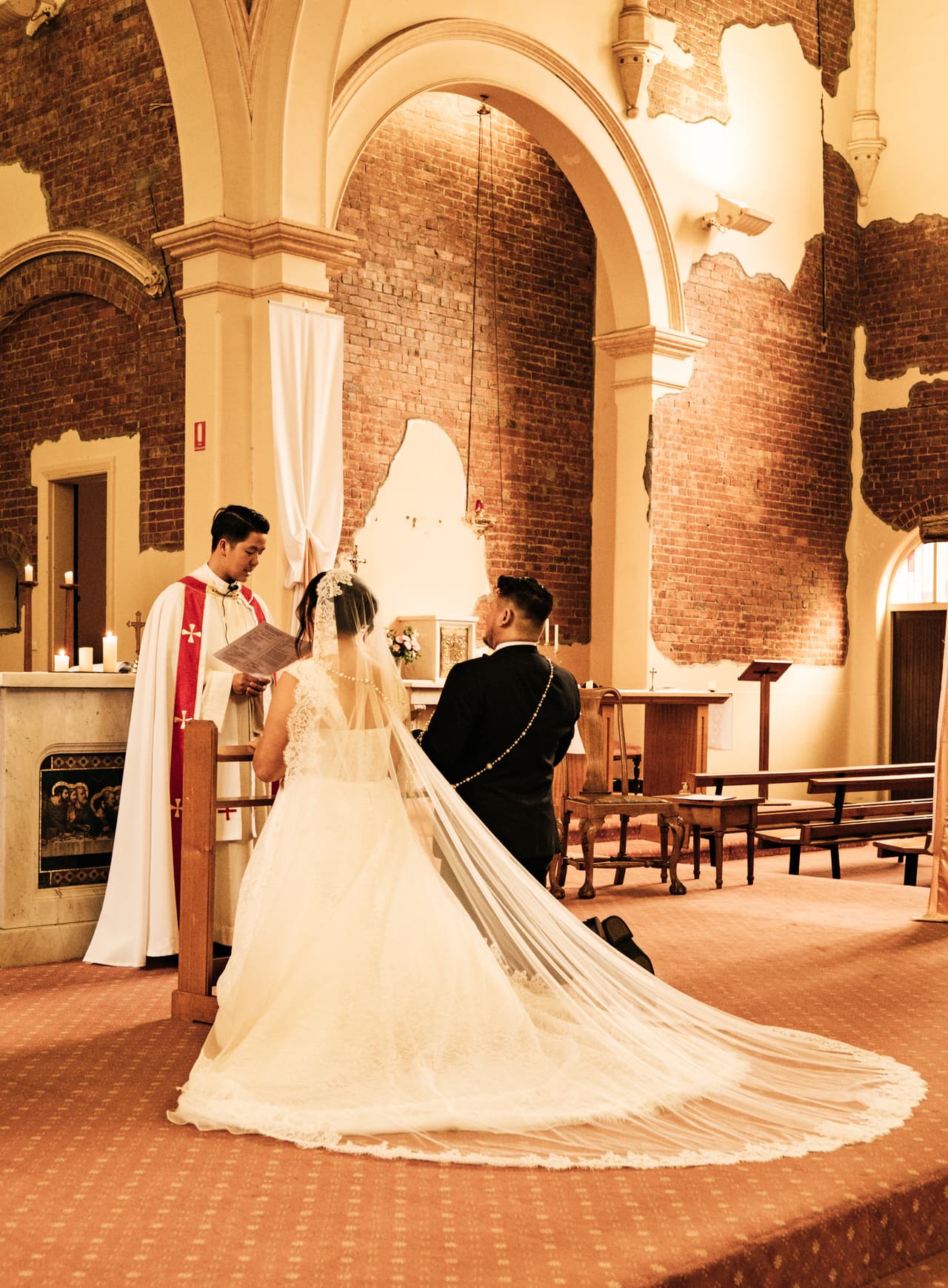 Ashley’s veil and train spread across the sanctuary floor as they stand before the priest