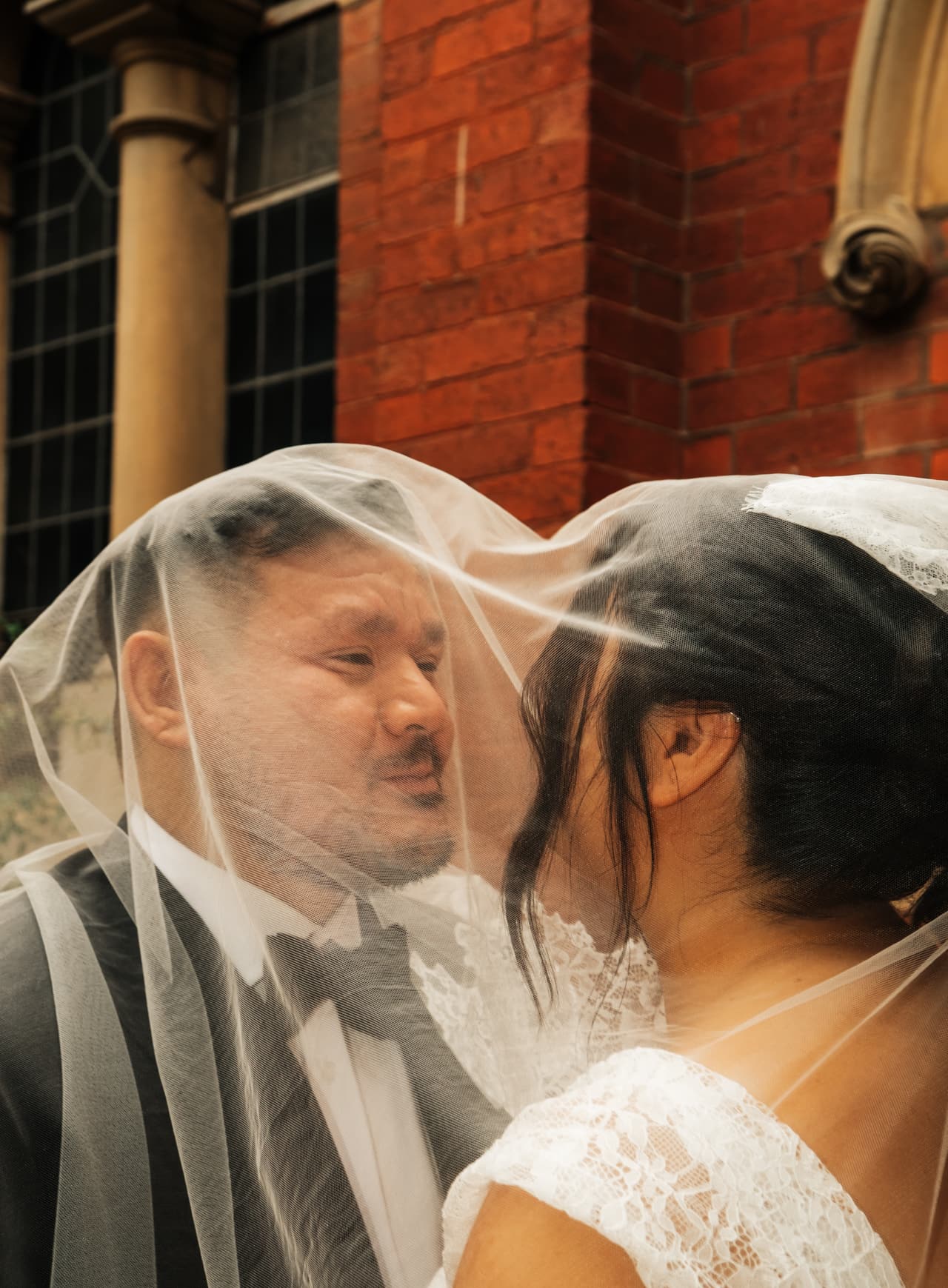 Ashley and Bryan kissing under her veil beside the brick arches of the church