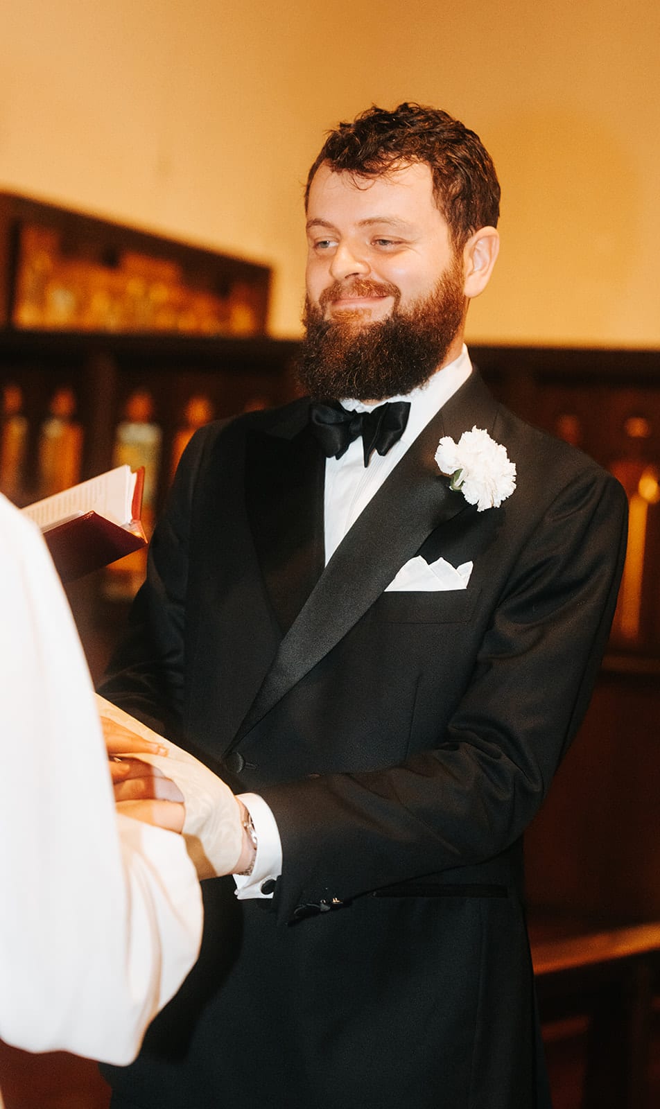 Aidan smiling at Bianca at the altar, a white flower in his lapel