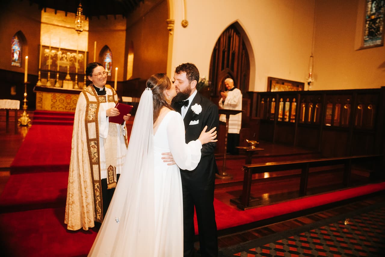 Bianca and Aidan kissing at the altar beneath the church's gold reredos