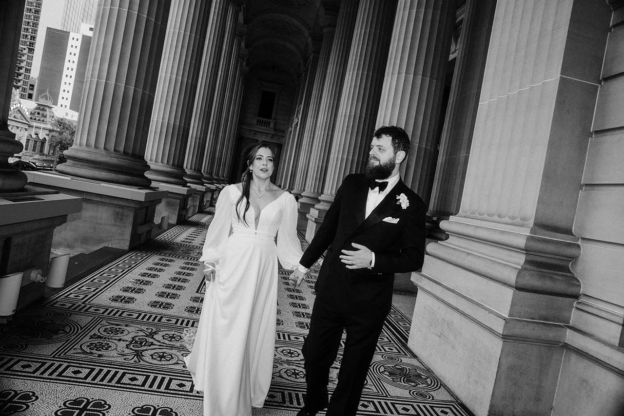 Black and white photo of Bianca and Aidan walking out between the columns, Aidan smiling