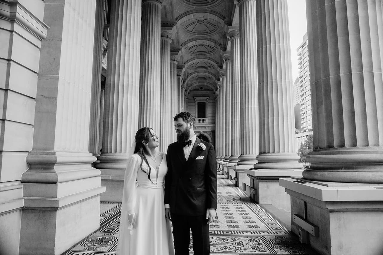 Black and white photo of Bianca and Aidan small among the tall columns of the Parliament House colonnade