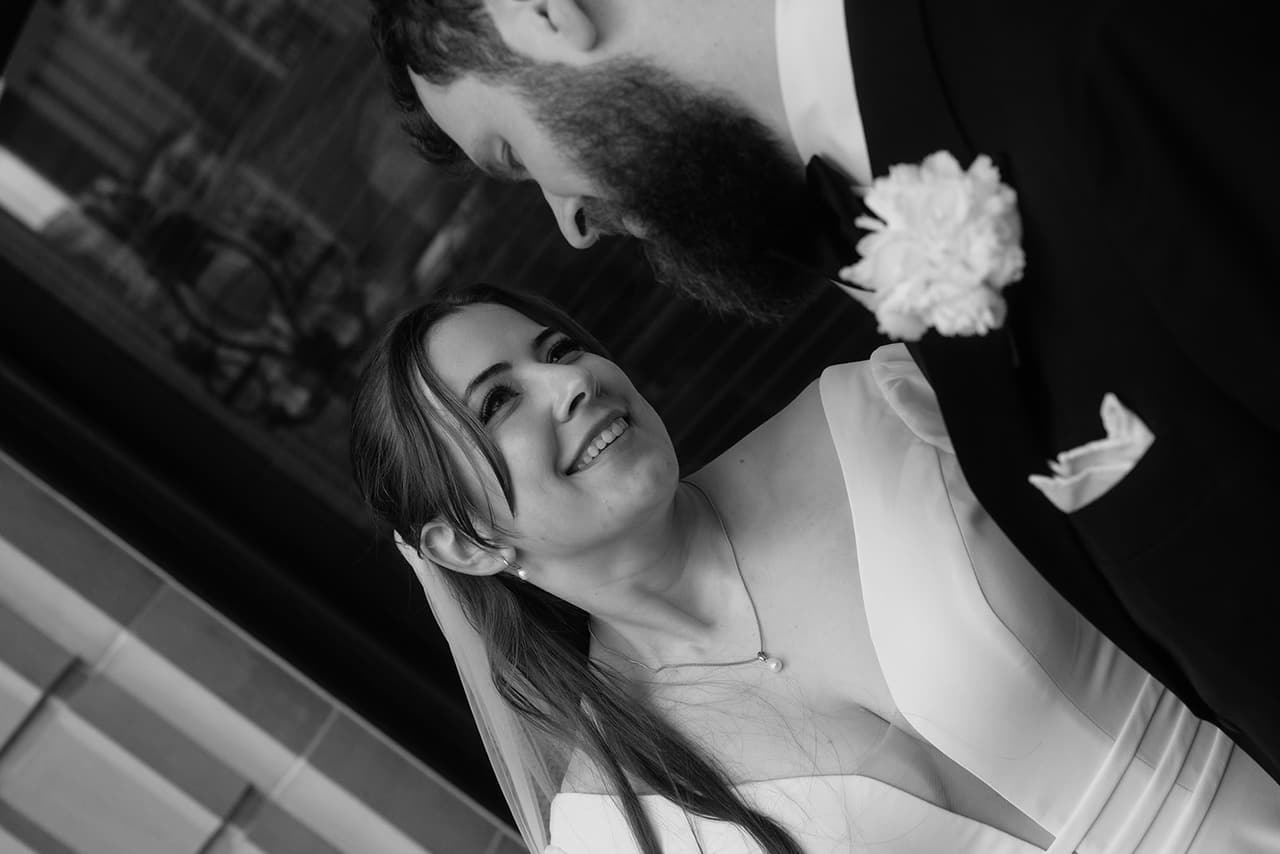 Black and white close up of Bianca laughing up at Aidan beside his white buttonhole