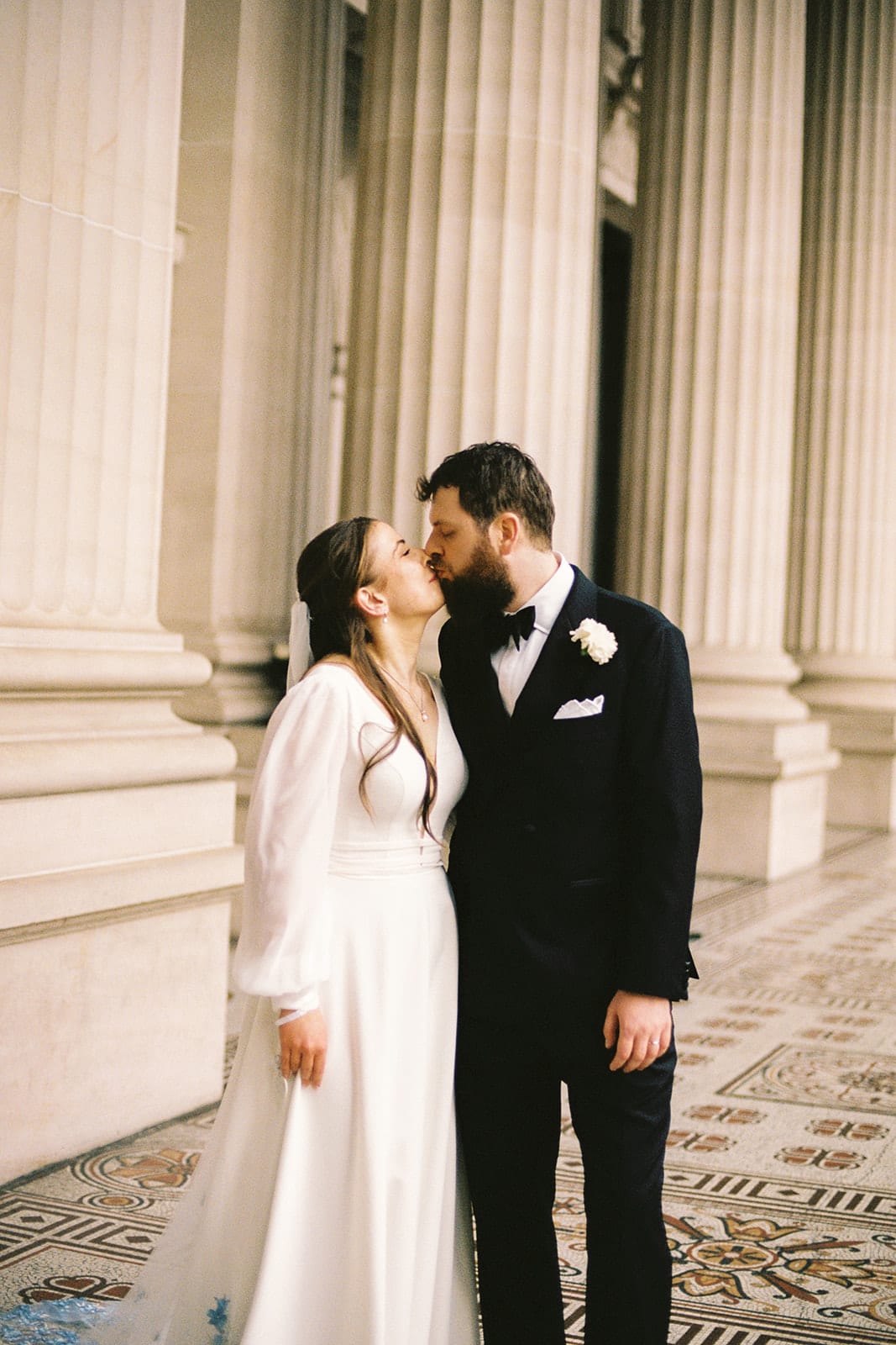 Bianca and Aidan kissing between tall sandstone columns, on 35mm film