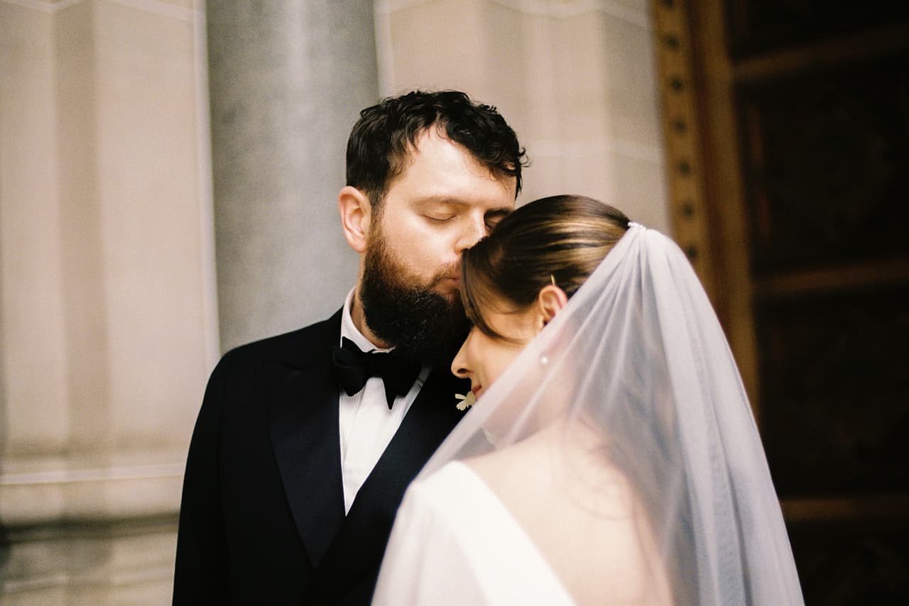 Aidan kissing Bianca's temple beside a stone column, on 35mm film