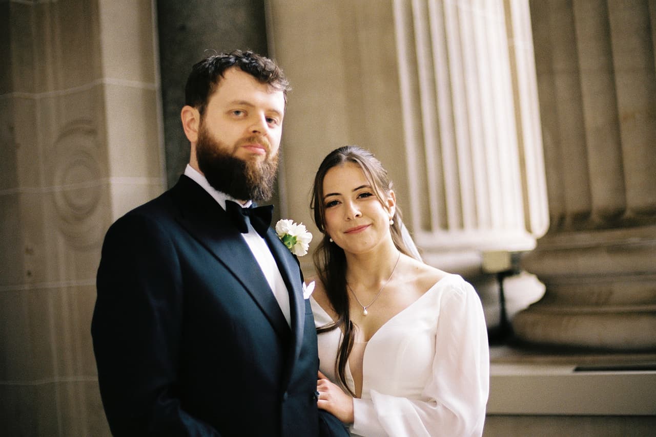 Aidan and Bianca standing side by side beside a sandstone column, Bianca smiling, on 35mm film