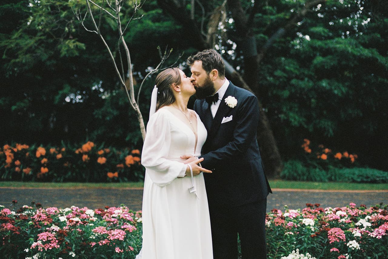 Bianca and Aidan kissing in front of the flower beds, on 35mm film