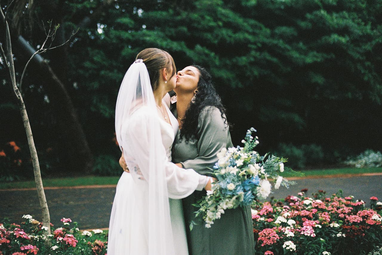 A friend in green kissing Bianca on the cheek beside the flower beds, on 35mm film