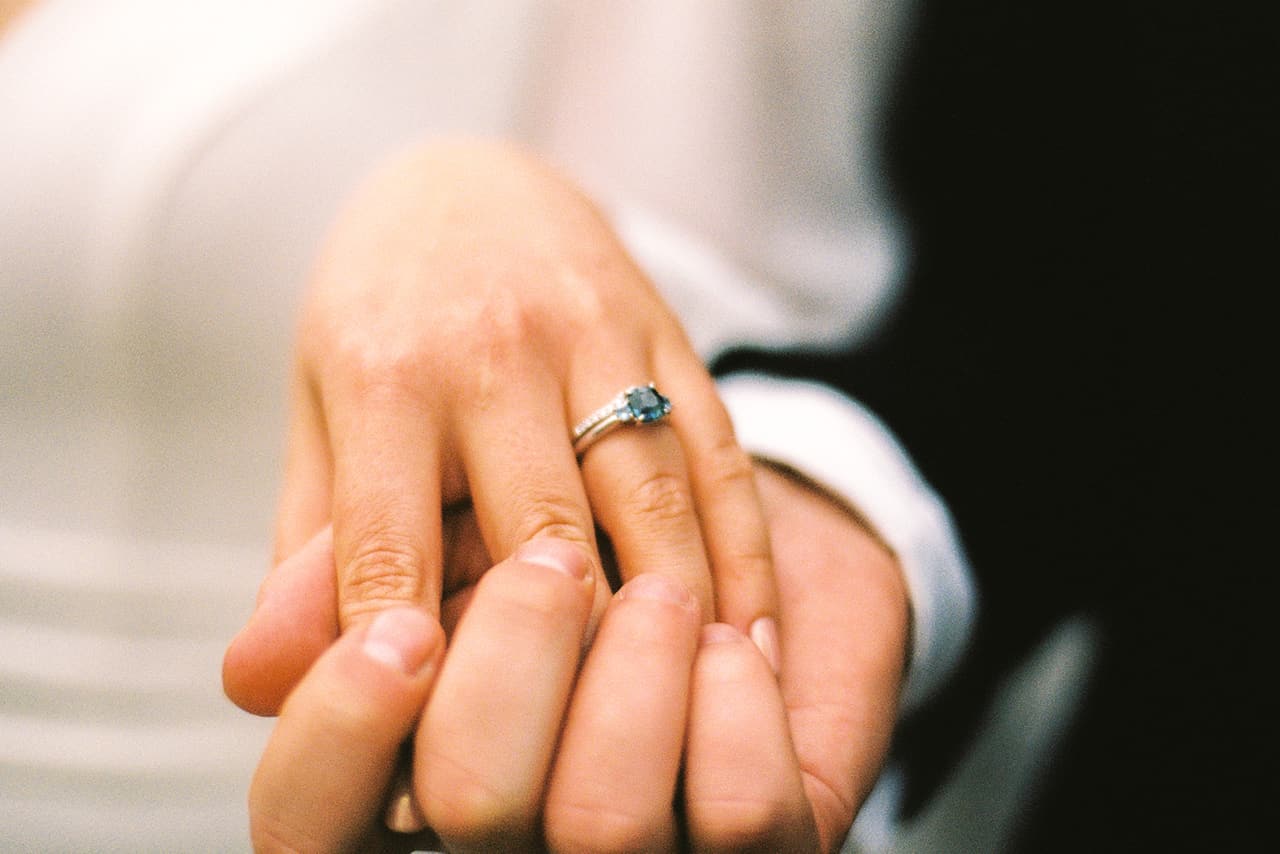 Close up of Bianca's hand in Aidan's, her rings catching the light, on 35mm film