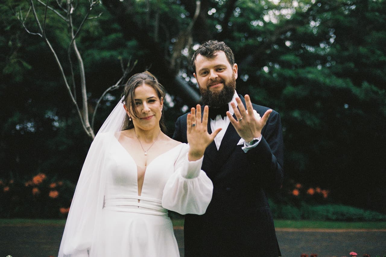 Bianca and Aidan laughing as they show their rings in the garden, on 35mm film