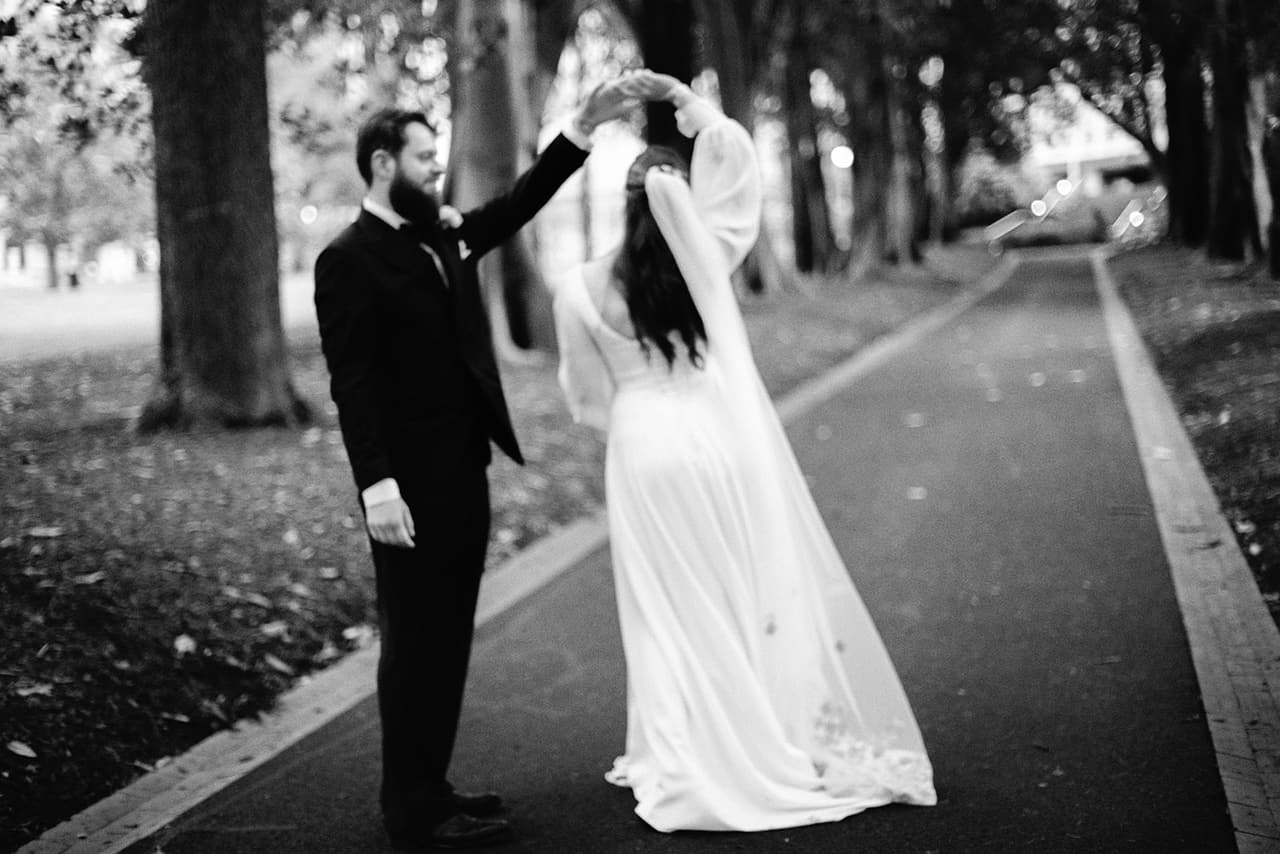 Black and white photo of Aidan lifting Bianca’s veil as she turns on the avenue path, on 35mm film