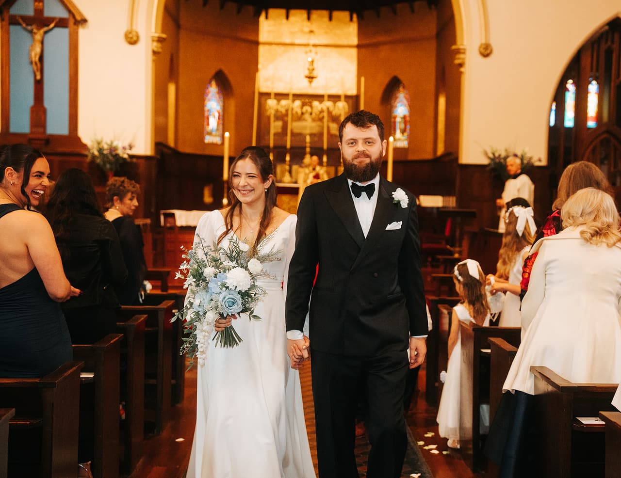 Bianca and Aidan walking back down the aisle past their guests, her bouquet in hand