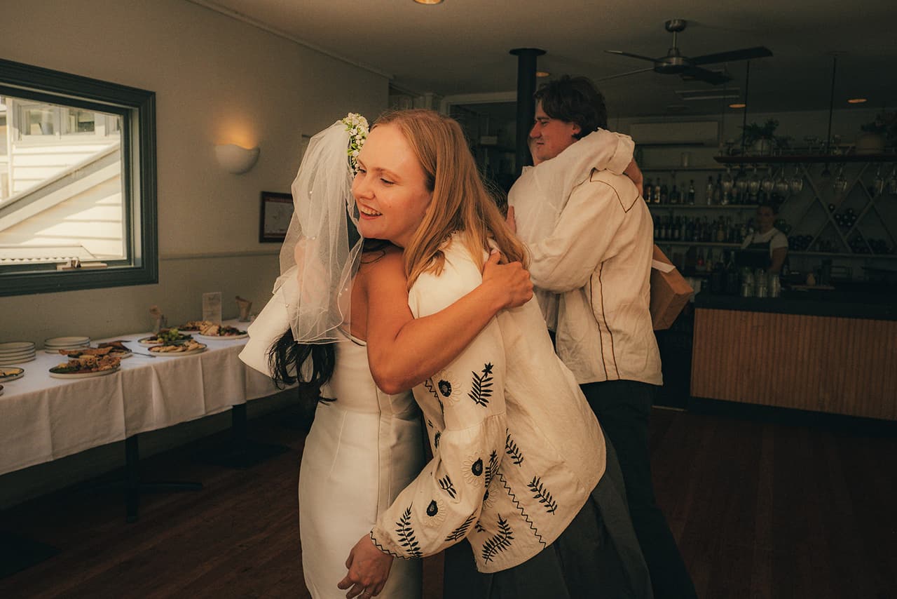 Cecile hugging a friend in an embroidered jacket inside the boathouse