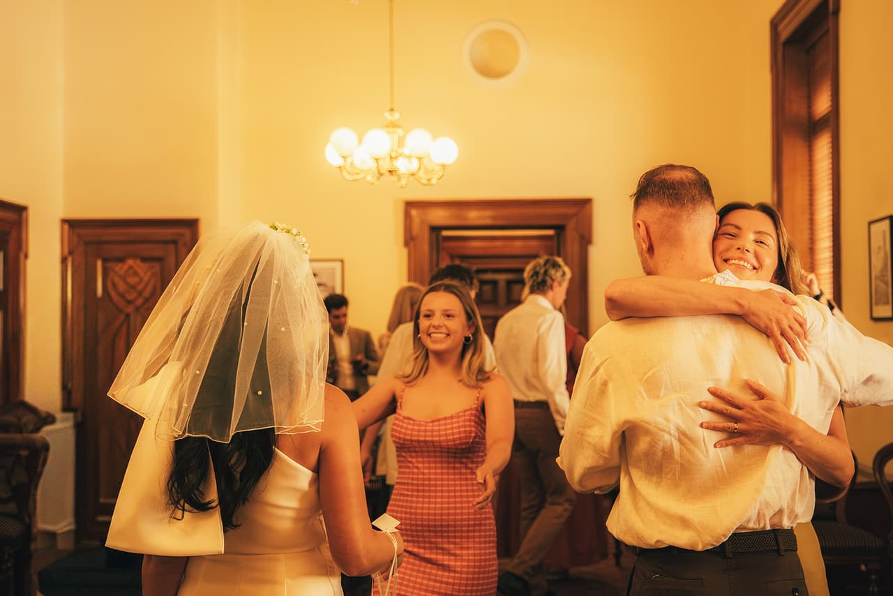 Stefan hugging a friend while Cecile, in her veil, greets another guest under the chandelier