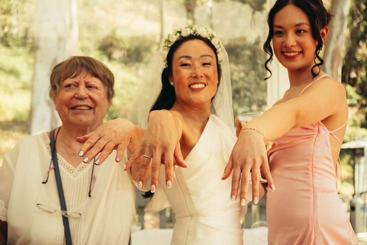 An older guest, Cecile and a friend holding out their hands to show their rings