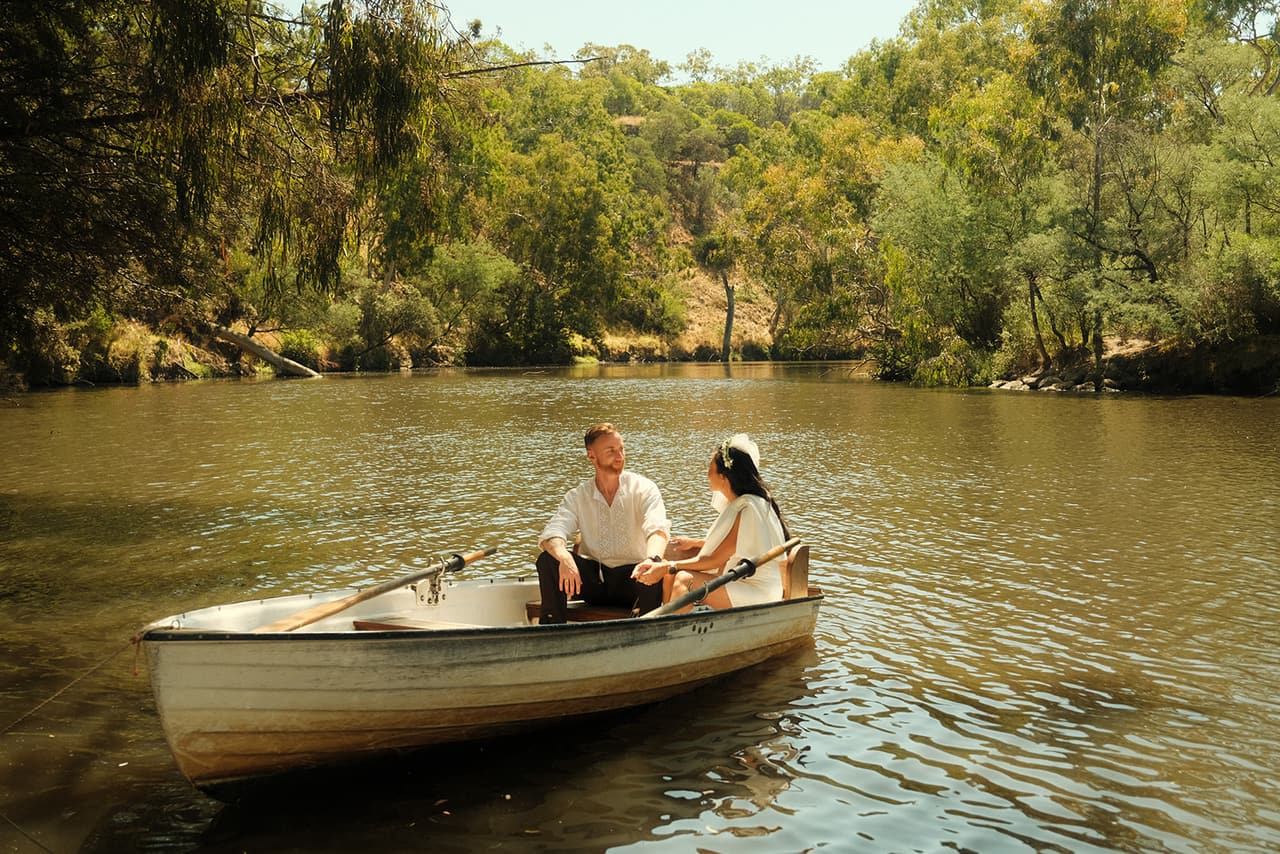 Cecile and Stefan in a rowing boat on the river, the bush thick on the banks