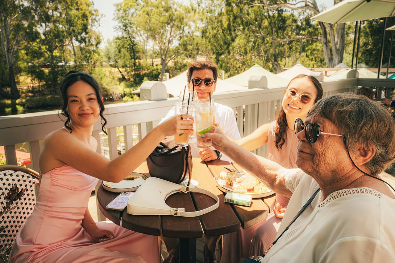 Friends raising their glasses around a table on the boathouse verandah