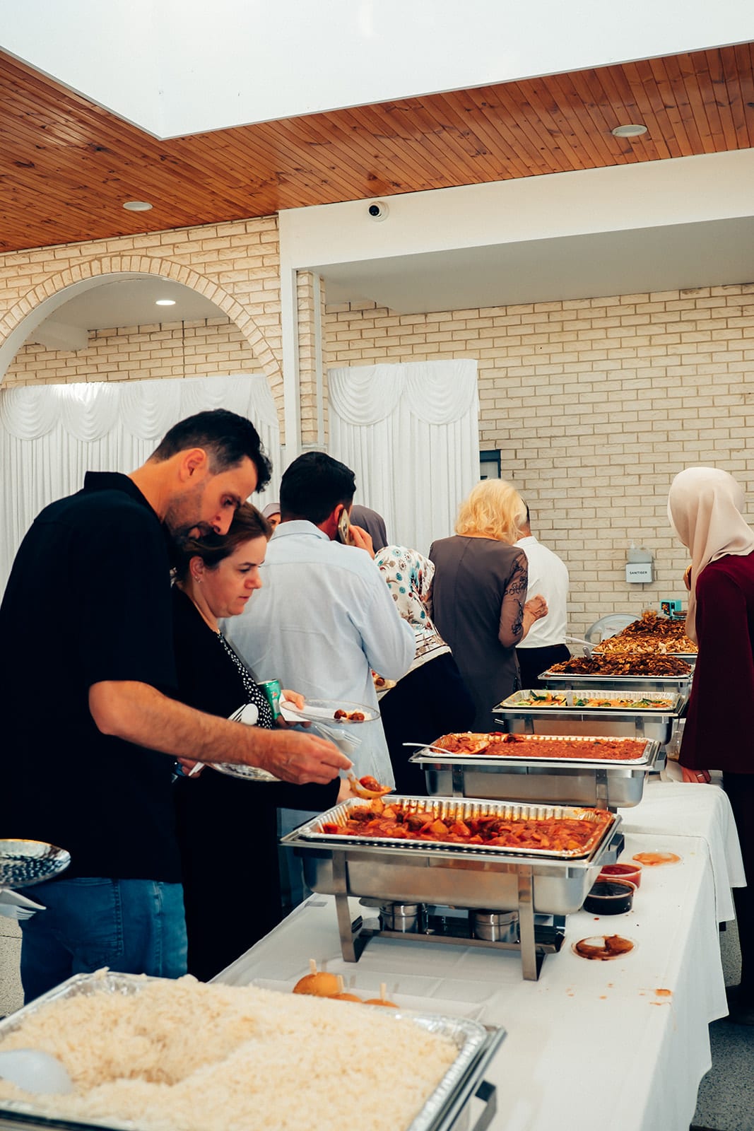 Guests serving themselves from trays of hot food at the buffet in the hall