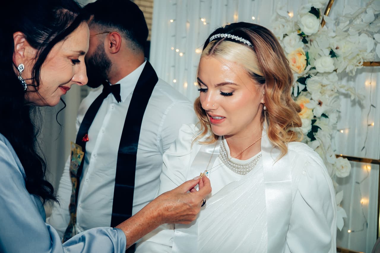 An older guest pinning gold onto Elektra as Yasir looks on