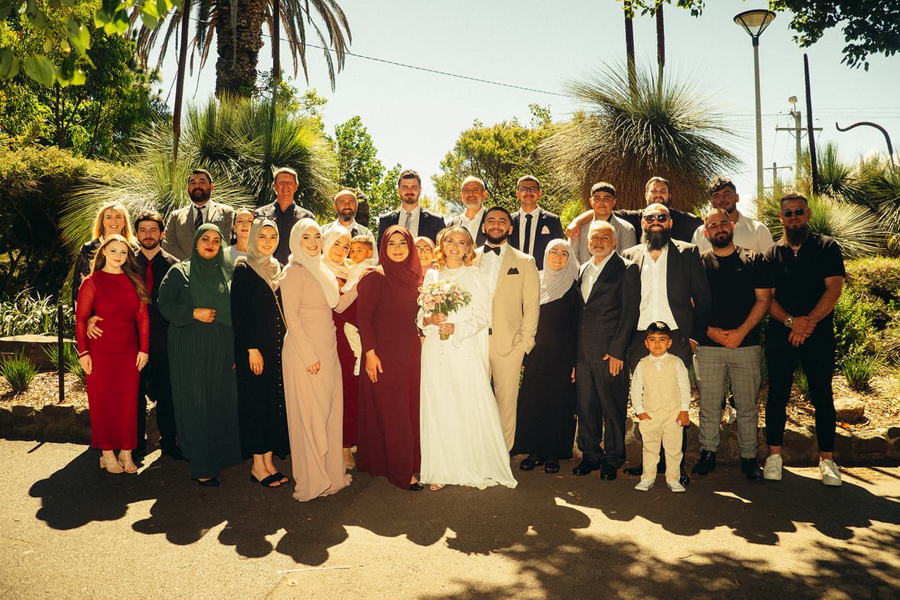 Elektra and Yasir with a big group of family and friends in the garden, grass trees and a palm behind them